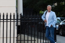 Phil in a blue suit standing against railings,